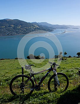 A bicycle leaning against a fence, at the background a view at the Otago Peninsula near Dunedin in New Zealand on a sunny day