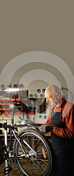 Bicycle Maintenance Concept. Old male mechanic or repairman working in a motorcycle repair garage, cleaning a wheel from