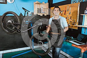 bicycle mechanic in smiling apron holding bicycle with thumbs up while standing beside bicycle