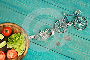 bicycle model, fresh vegetables and centimeter tape on blue wood