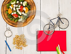 bicycle model, salad of fresh vegetables, red notepad, stopwatch