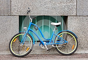 A bicycle parked against the wall of the house, secured by an anti-theft chain to the window bars. Wall, sidewalk. Photo.