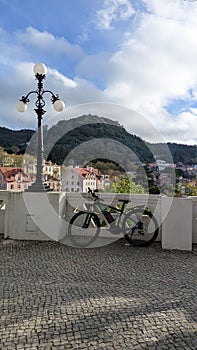 The bicycle is parked near a concrete railing next to an iron lamppost against the backdrop of mountains overgrown with