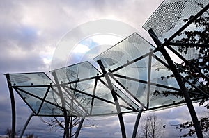 Bicycle parking shelter with glass roof with dotted print. Construction from bent gray tubes into an arc. tempered laminated glass