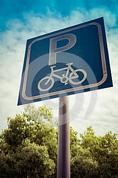 Bicycle parking sign on blue sky and tree with filter