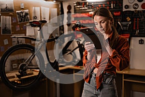 bicycle repair. Blonde woman using a digital tablet in a bicycle repair shop.