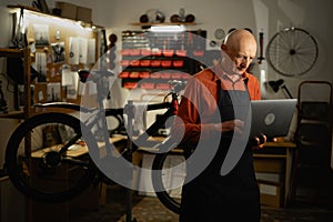 Bicycle repair shop owner, old mechanic with laptop working in his garage