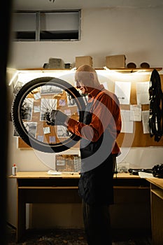 Bicycle repairing concept. Old mechanic holding bike wheel repairing bicycle in repair workshop