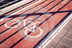 Bicycle sign on a red bike path under a shadow of a fence