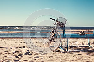 Bicycle stands near bench on beach against sea.