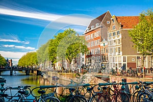 Bicycles on the bridge in Amsterdam, Netherlands against a canal and old buildings during summer sunny day. Amsterdam postcard