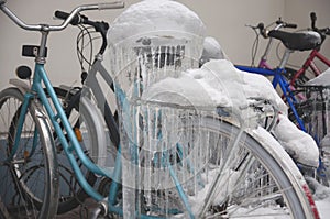 Bicycles covered with ice, big icicles and snow stand at parking near house