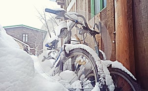 Bicycles covered with snow stand against a wooden wall near the house. Old abandoned bicycles in the backyard of a house
