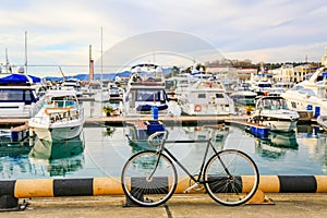 Bicycles parked on pier. Motor boats and luxury yachts docked in sea port. City street and blue water. Summer holiday vacation.