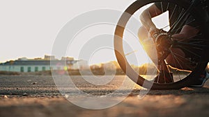 Bicyclist inflates rear flat tire by compact hand pump at sunset, punctured wheel, broken bicycle out of town outside