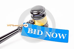 Bid now text on paper tag with wooden gavel auction.