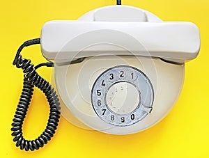 Biege old telephone with rotary dial on yellow background. Flat lay