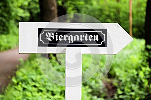 Biergarten Beer Garden in German white wood arrow direction sign with traditional German writing font. Sign in open air