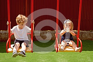 A big adventure playground. Girl and boy haircut styles. Small children with blond hair on swing. Small brother and