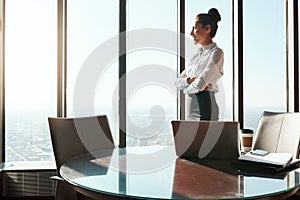 Big ambitions are always running through her mind. a young businesswoman looking out the window in an office.