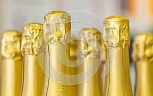 Big amount of golden champagne bottles necks and top caps at standing the light background