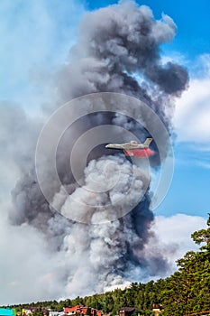 Big amphibious fire aircraft drops water on large forest fire near the village