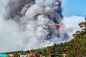 Big amphibious fire aircraft drops water on large forest fire near the village