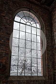 Big, arcade window with muntins in a shabby, brick wall. Industrial interior. Winter scenery outside the window