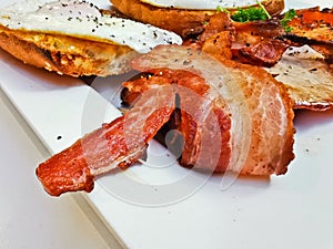 Big bacon in English breakfast with sunny fried eggs, bacon, tomatoes, ham on Turkish flat grilled bread on white dish