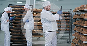 In a big bakery industry main baker take photo from a big tablet of a fresh baked bread from shelves while other two