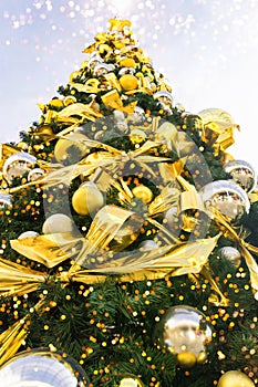 Big beautiful Christmas tree decorated with ornaments golden silver hanging balls bows garland sparkling lights in european city