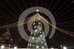 big beautiful Christmas Tree with decorations and Illuminations in snowy night against the background of Orthodox church. New Year