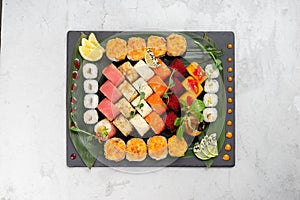 Big beautiful set of different types of sushi maki on a black rectangular stone slate plate.