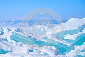 Big Beautiful turquoise blue ice on the Frozen Lake Baikal with mountains on the background.