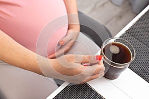 Big belly of a pregnant girl and a cup of coffee in her hand. The benefits and harms of coffee for pregnant women.
