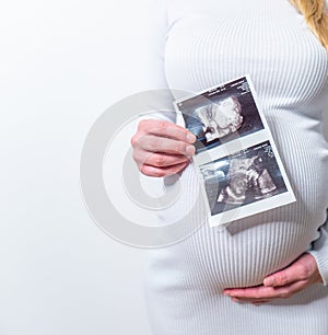 Big belly of pregnant woman holding the ultrasound film on her stomach with drawing kids face