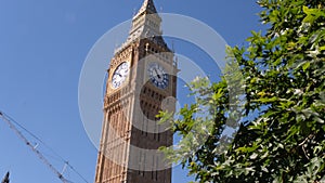 Big Ben clock tower close up in London on the blue sky and green tree. Symbol of London, United Kingdom.