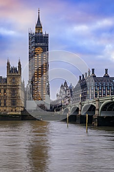 Big Ben covered in scaffolding for restoration and Portcullis House across Thames river before sunset in London, England photo