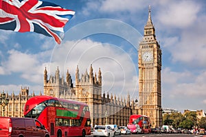 Big Ben with red buses on the bridge against flag of England in London, England, UK