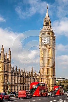 Big Ben with red buses on the bridge during sunny day in London, England, UK