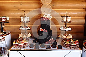 Big black birthday cake with fresh fruits and sweets on a festive table. Candy bar. Table with different sweets for party