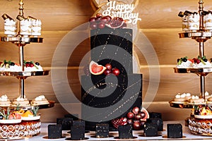 Big black birthday cake with fresh fruits and sweets on a festive table. Candy bar. Table with different sweets for party