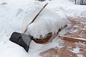 Big black plastic shoveling with wooden handle in snow. Cleaning of snow after heavy snowfall from steps. Very large snowdrifts.