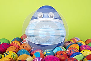 Big blue egg with face mask between painted easter eggs before gren background