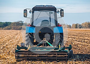 Big blue tractor plows the field and removes the remains of previously mown corn.