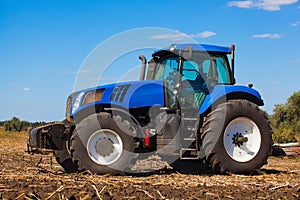 Big blue tractor plows the field and removes the remains of previously mown sunflower. photo