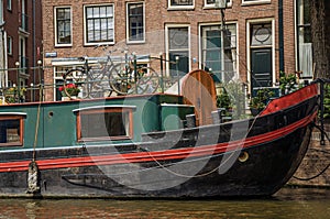 Big boat moored at side of tree-lined canal, old buildings and sunny blue sky in Amsterdam.