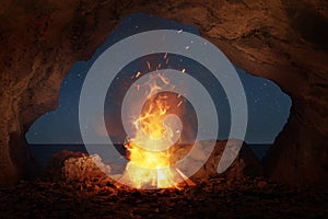 big bonfire with sparks and particles in front of sea and cave