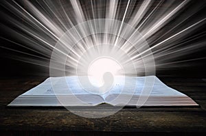 The big book of the Bible lies on a wooden table. In the dark. A light shines on the book from above. Light comes out of the book photo