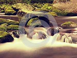 Big boulders covered by fresh green moss in foamy water of mountain river. Light blurred cold water with reflections, white